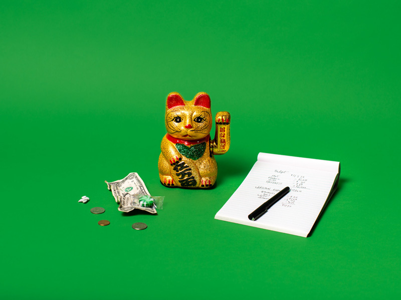 Gold lucky cat figurine beside cash, coins and a notepad