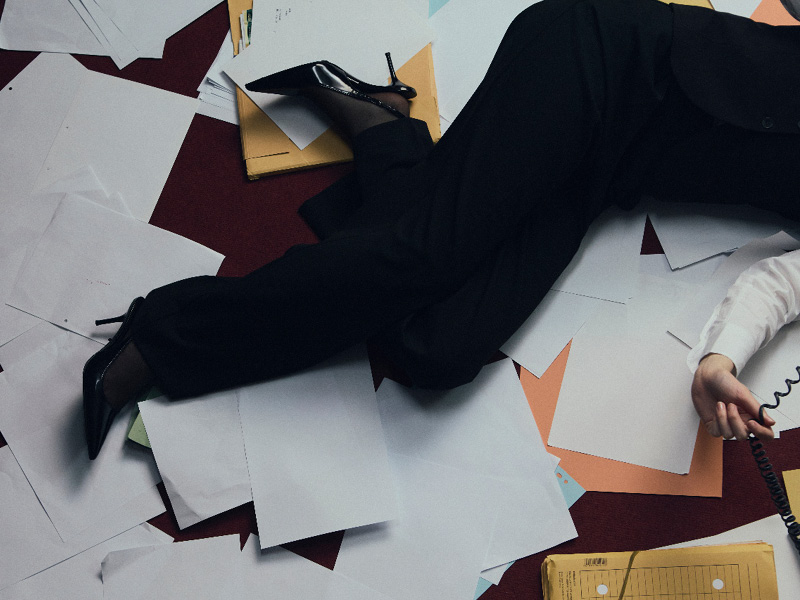 Person lying on a floor covered in paper, holding a phone receiver