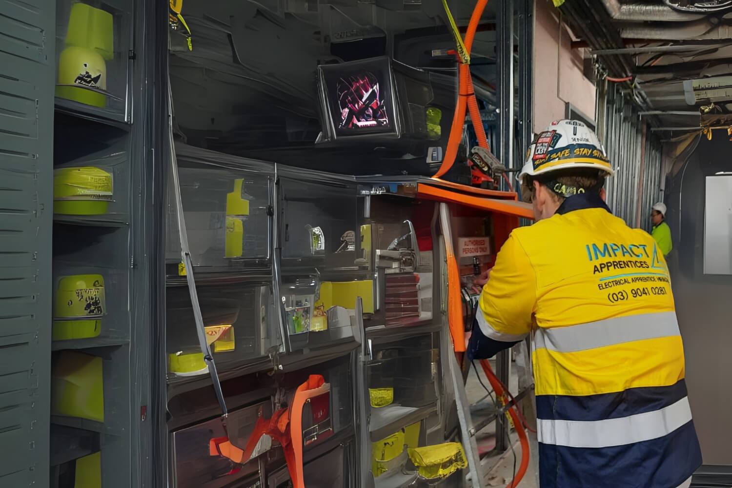 An electrical apprentice who is part of Impact Apprentices Pty Ltd. working on a switchboard panel during his apprenticeship wearing his safety equipment.