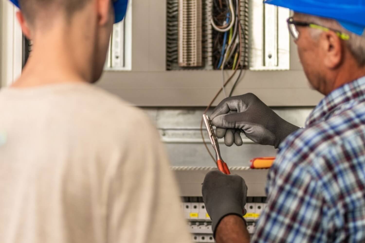 Senior electrician teaching his male apprentice how to strip the wires in the distribution board.