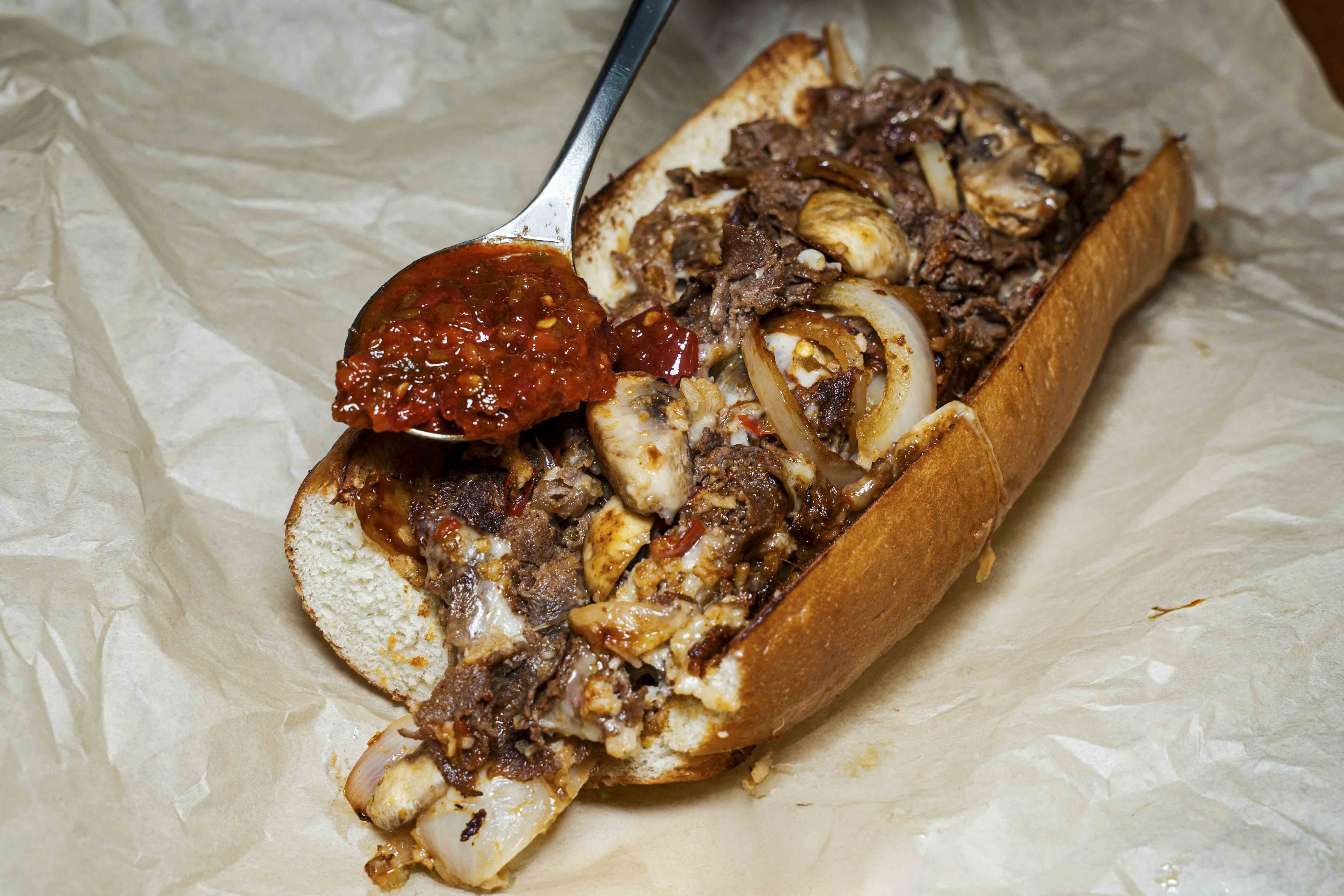 A cheesesteak sandwich loaded with grilled onions, roasted garlic, mushrooms, chopped calabrian peppers, and white american cheese.