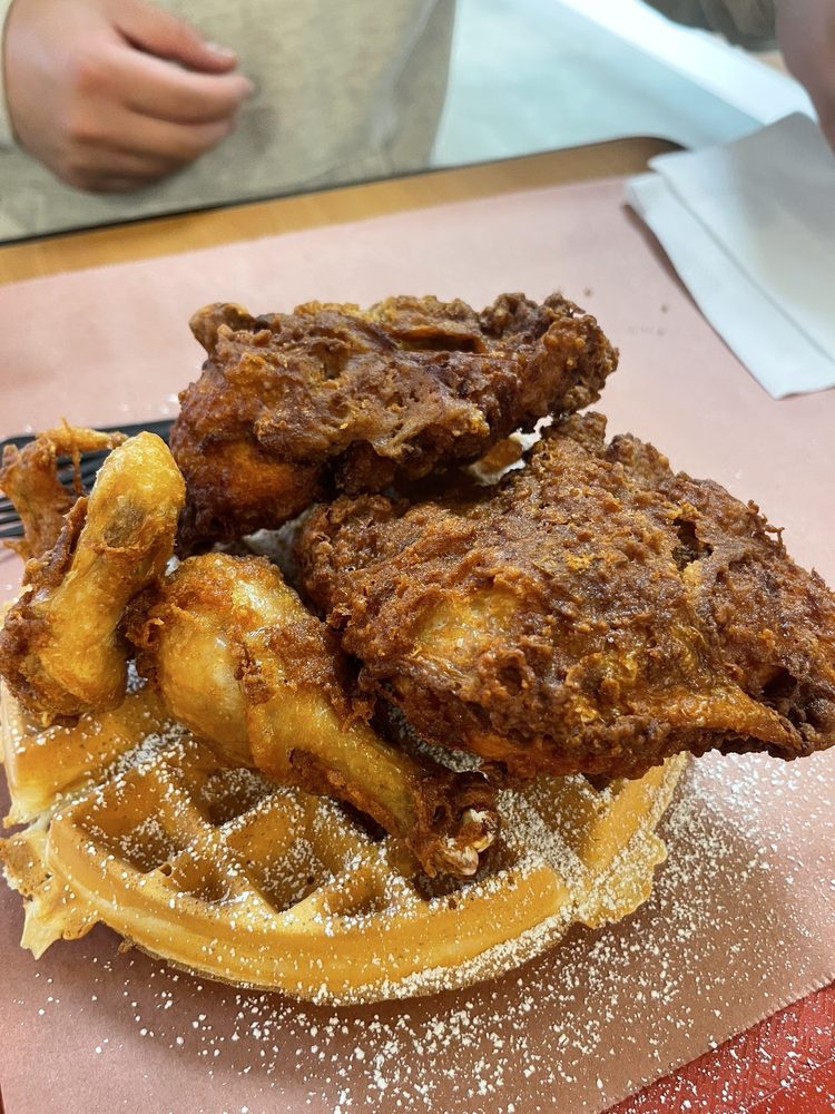 A diner's photo of a bed of crispy fried chicken on top of a fluffy waffle sprinkled with powdered sugar.