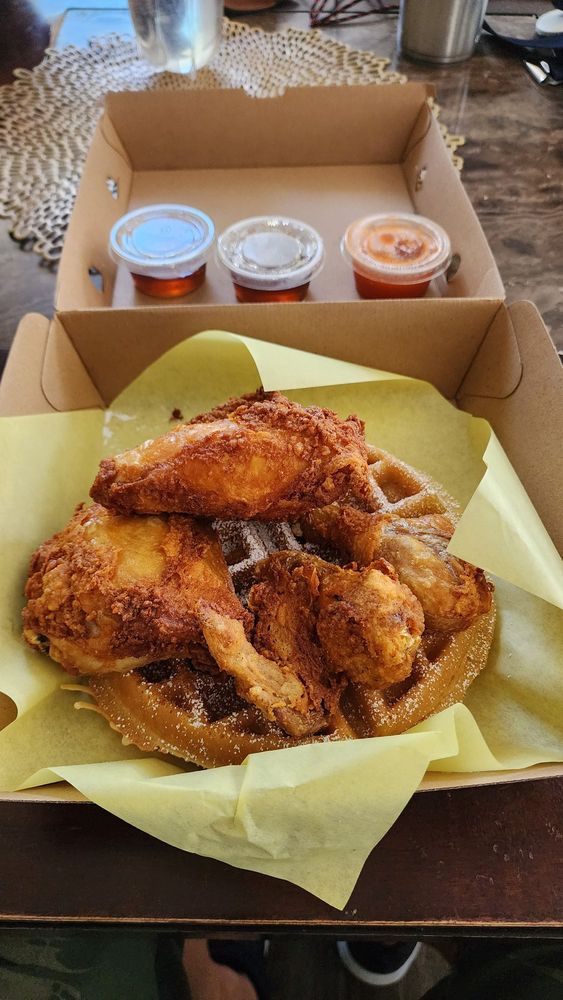 A photo of crispy fried chickien on top of a waffle, sprinkled with powdered sugar
