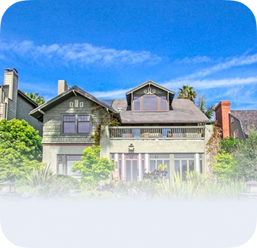 An image of a two-story green house in Long Beach with balcony and front garden.