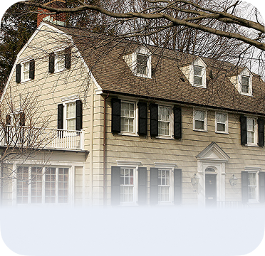 An image of a large beige colonial-style house in Amityville with black shutters and dormer windows