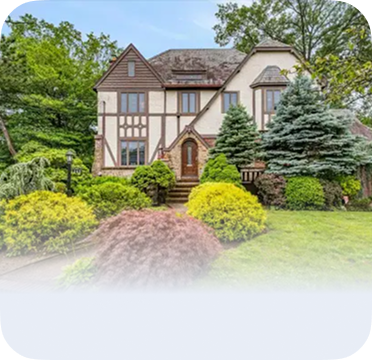 An image of a Tudor-style house in Woodmere with landscaped front yard and tall trees.