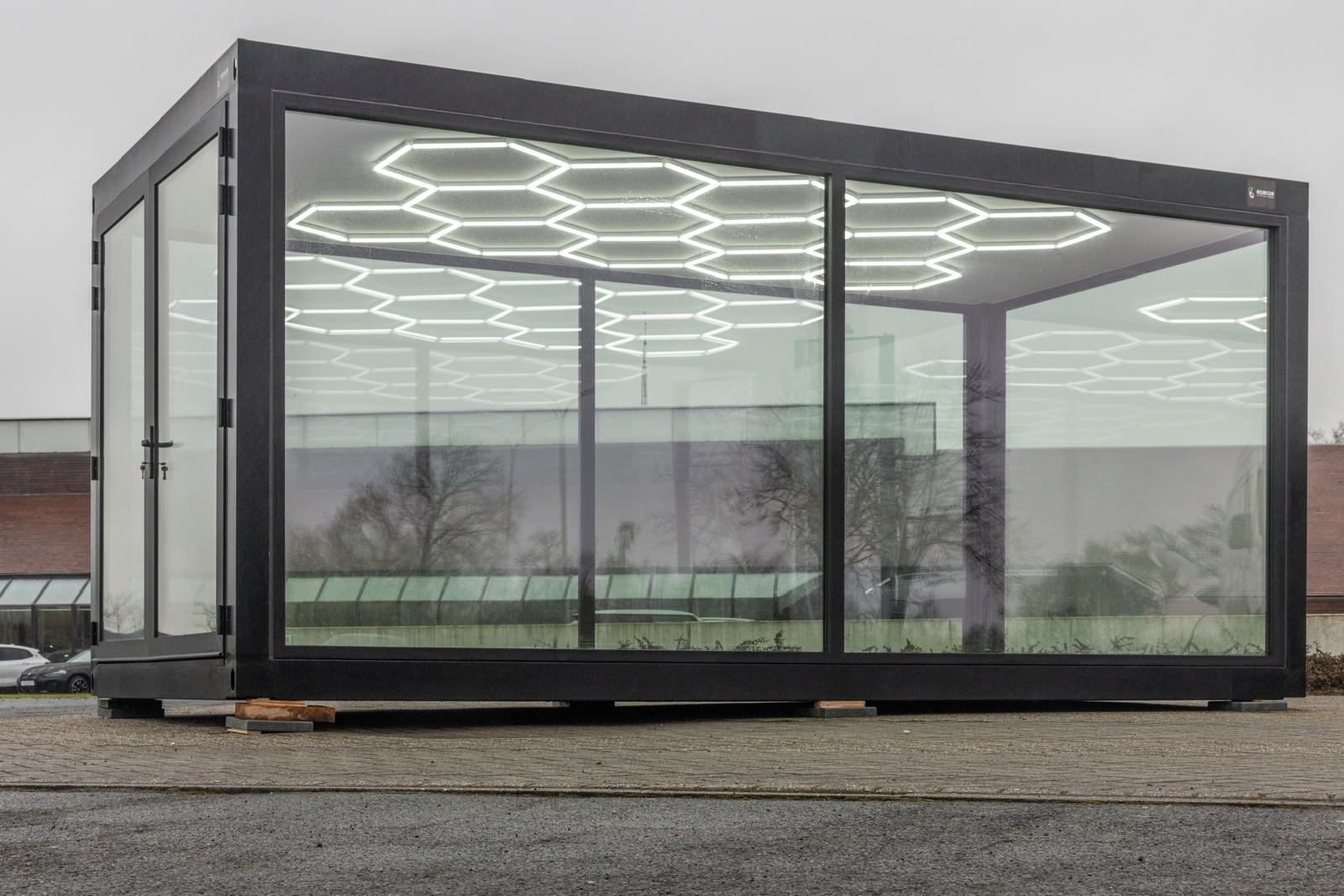 Een modulaire unit van ROBCOR met glazen wanden en hexagonale LED-verlichtingspanelen. 