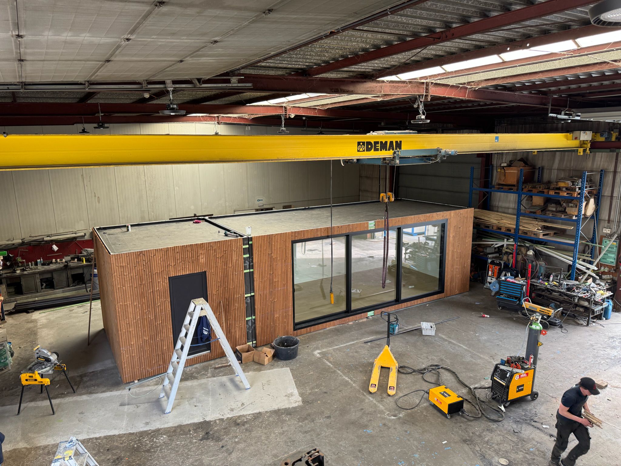 Een moderne houten unit in aanbouw in de werkplaats van ROBCOR, met zichtbare gereedschappen en apparatuur, inclusief een kraan boven het werk.