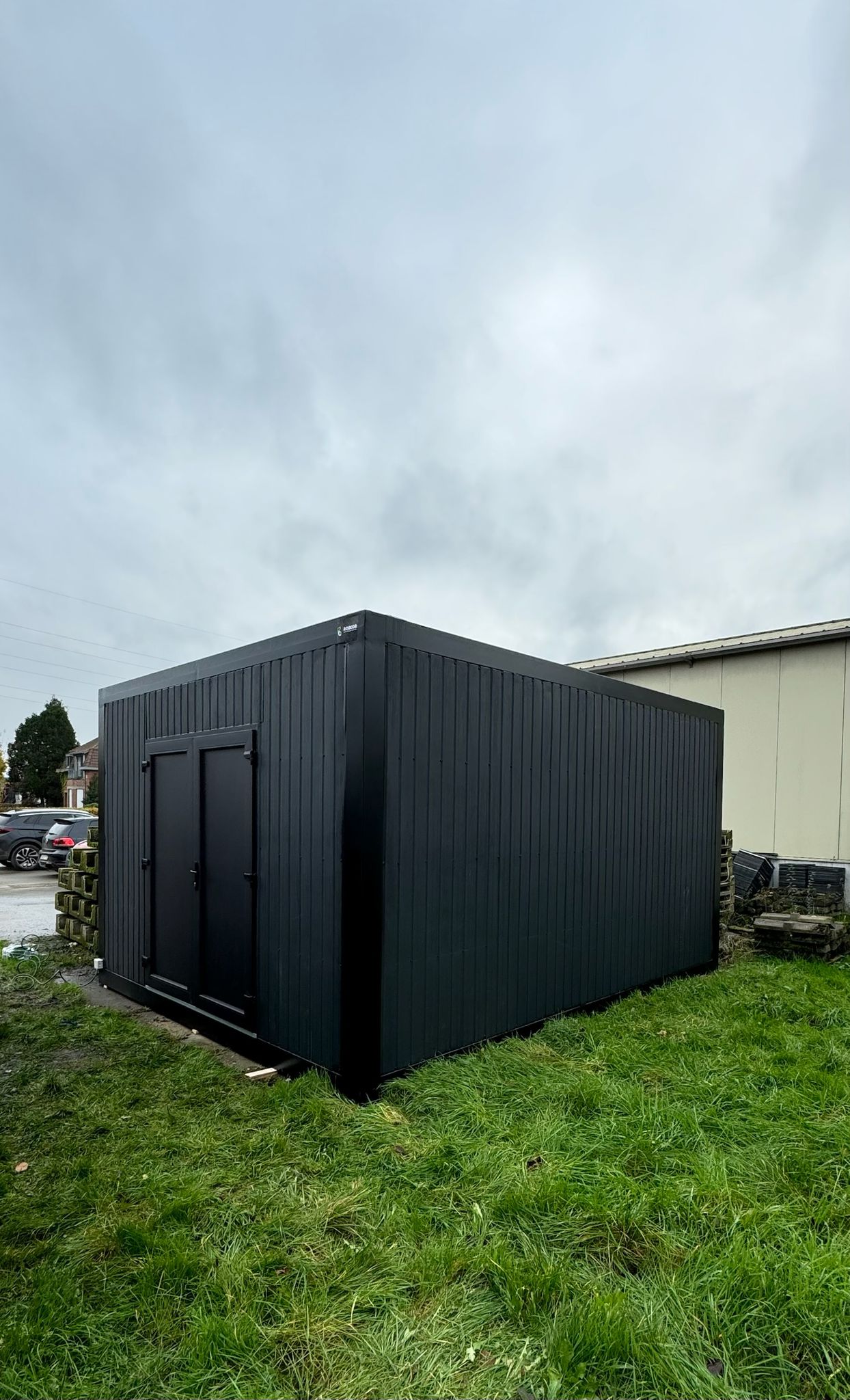 Zwarte, rechthoekige opslagcontainer van ROBCOR op gras onder een bewolkte hemel. De donkere kleur en de wolkenlucht benadrukken de sfeervolle, sombere uitstraling.