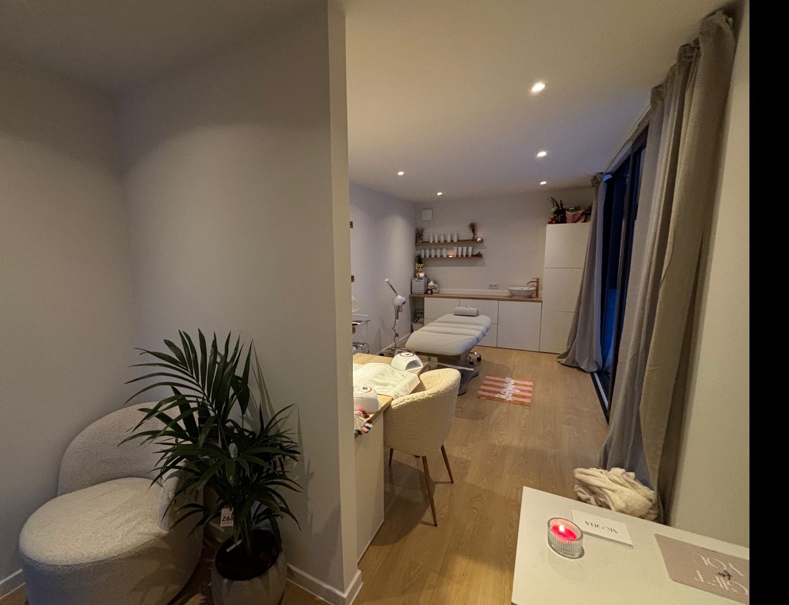 Moderne schoonheidssalon met behandelstoel, bureaustoel, planten en houten vloer.