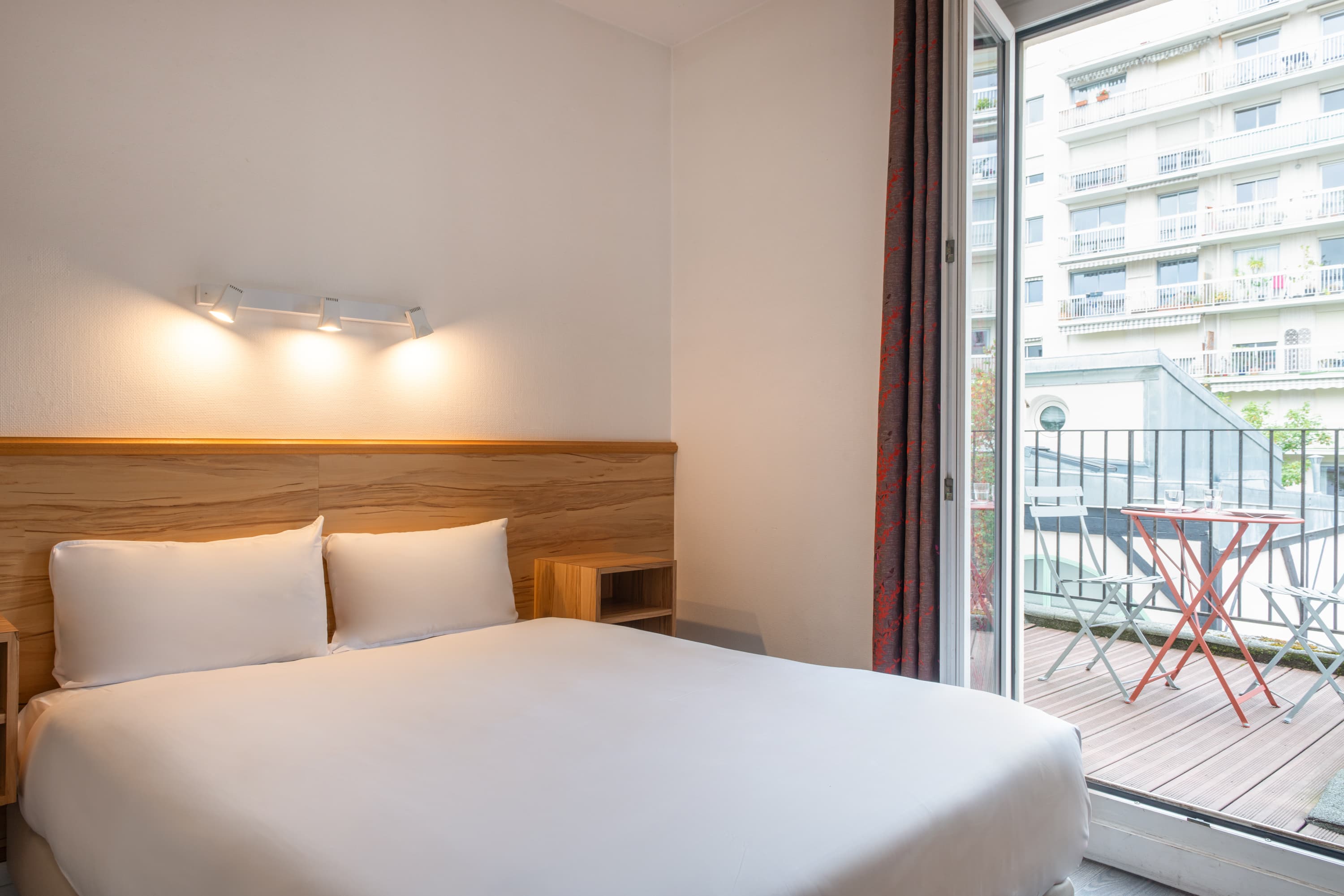 Image de studio de 15 m² avec terrasse pour 2 personnes avec kitchenette rouge et acier avec frigidaire, table à manger, et micro-onde. Ce studio contient aussi une salle de bain blanche avec douche, lavabo, miroir et toilettes. Il y a un lit double et une télévision.