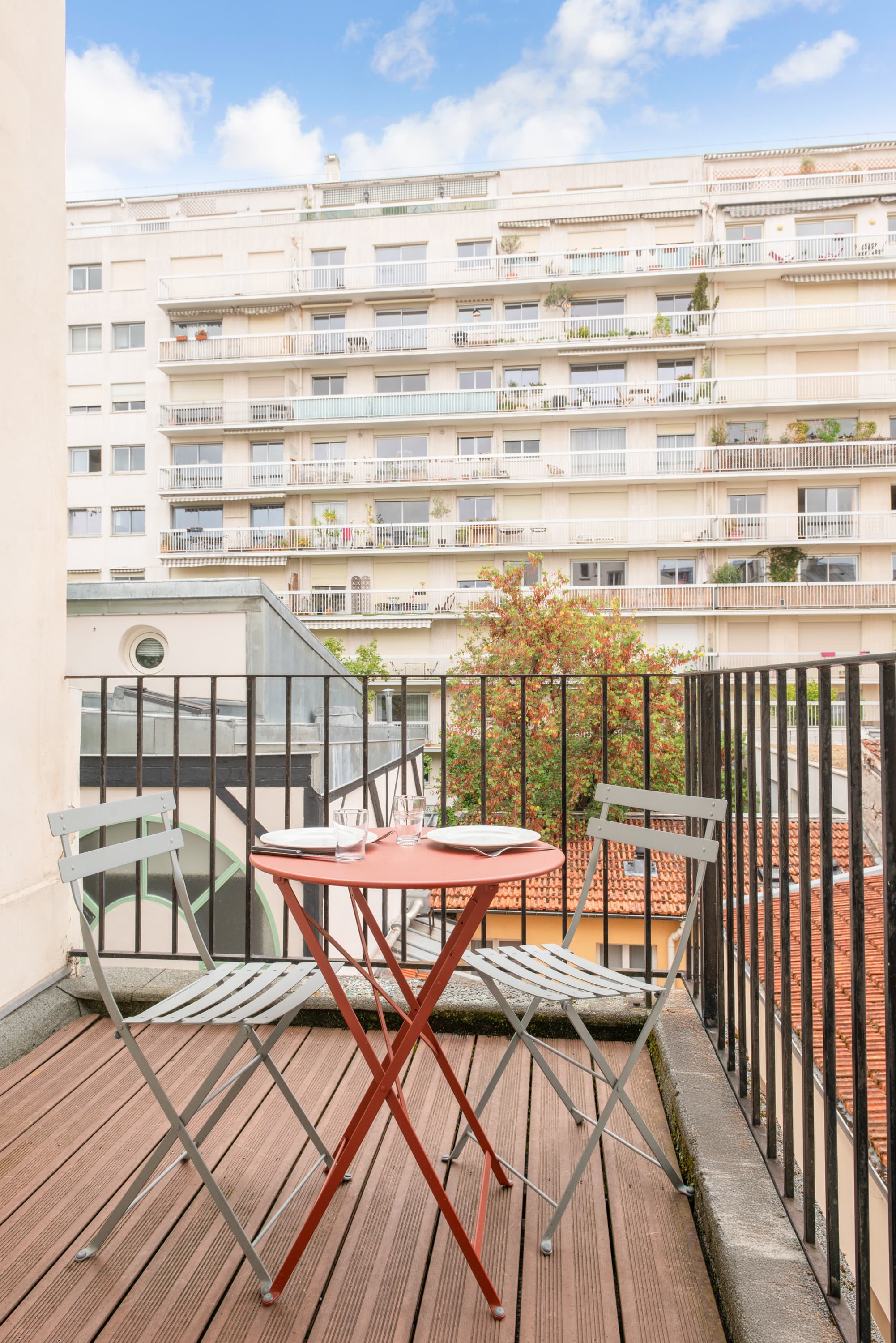 Image de studio de 15 m² avec terrasse pour 2 personnes avec kitchenette rouge et acier avec frigidaire, table à manger, et micro-onde. Ce studio contient aussi une salle de bain blanche avec douche, lavabo, miroir et toilettes. Il y a un lit double et une télévision.