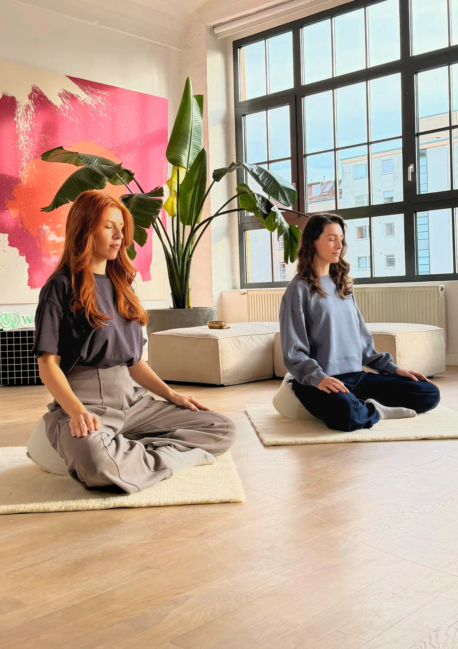 Zwei Frauen sitzen auf Meditationskissen und praktizieren eine Achtsamkeitsmeditation.