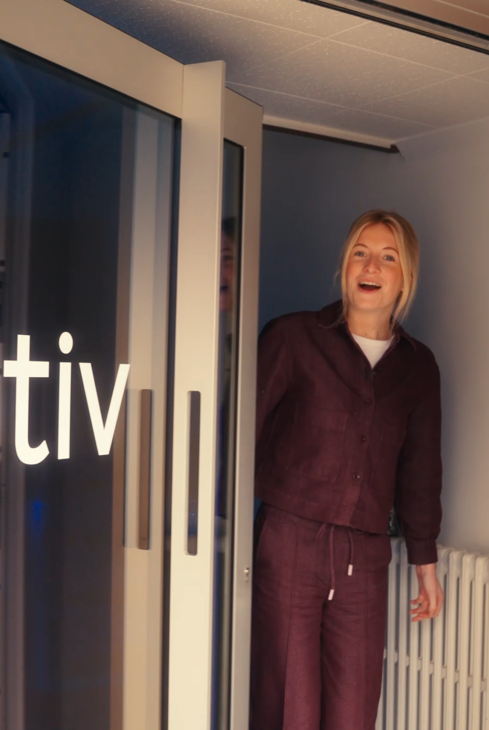 Smiling woman wearing maroon outfit standing in an open doorway with white radiators behind her.