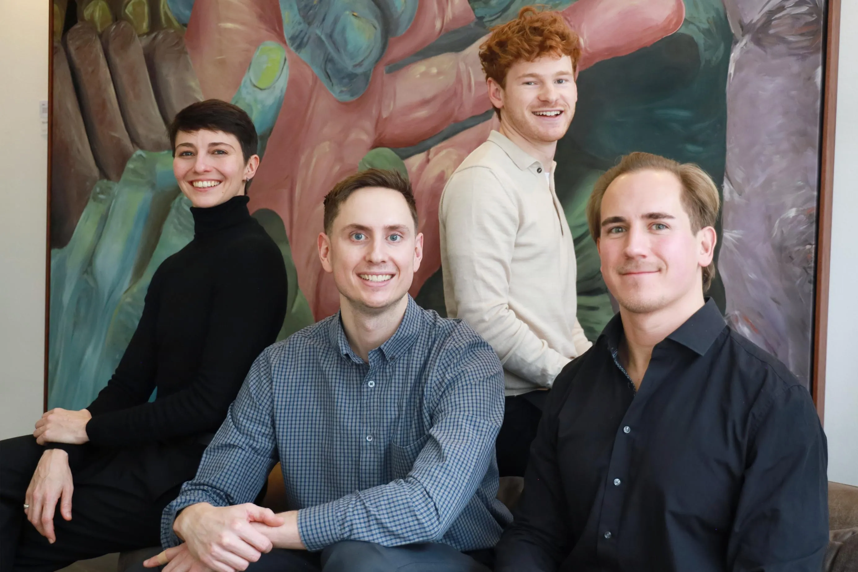 Vier lächelnde Personen vor einem großen farbenfrohen Kunstwerk mit Händen.