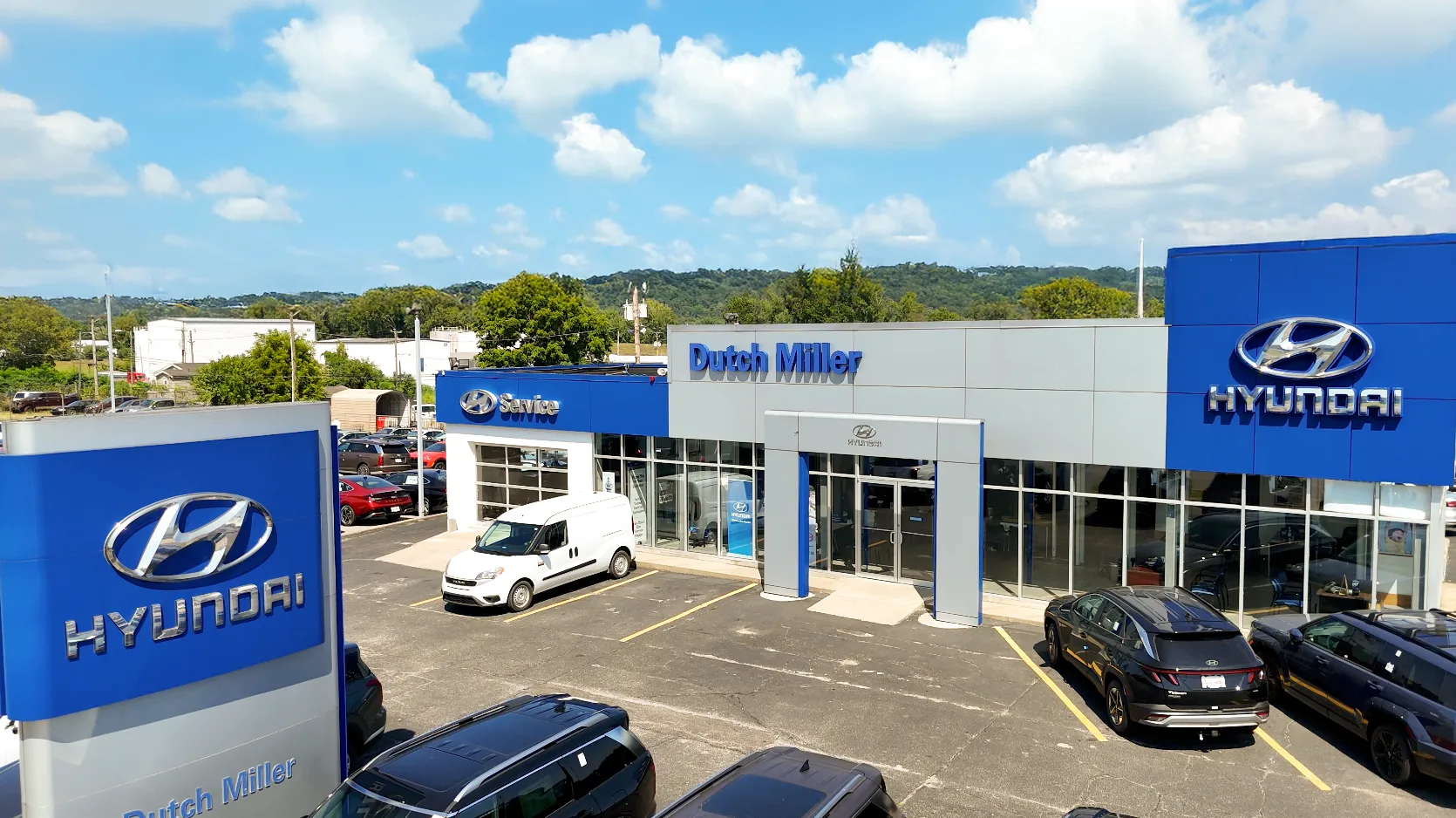Exterior view of Dutch Miller Hyundai car dealership with parked cars and a service area under a blue sky with clouds.