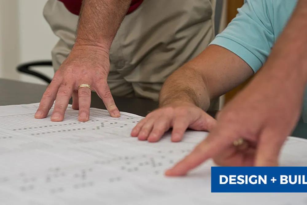 Three hands pointing and reviewing a large architectural blueprint on a table.