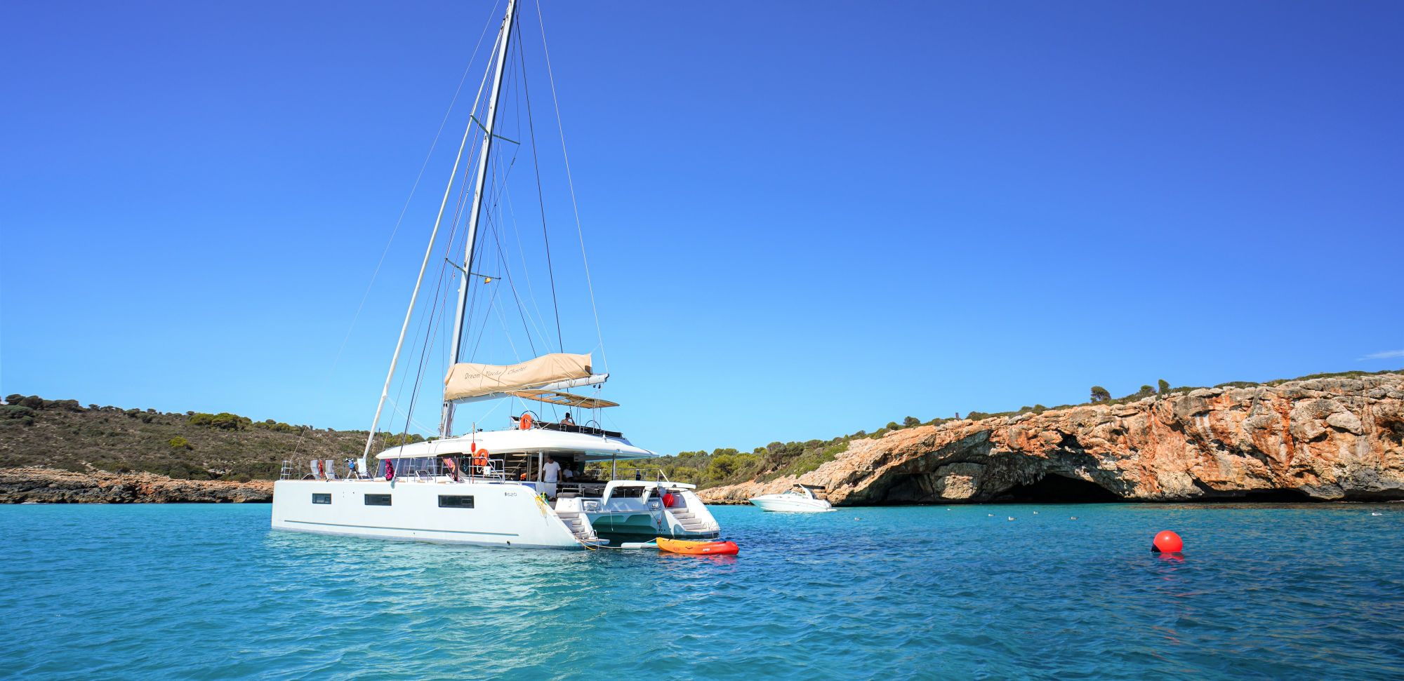 A luxury catamaran, anchored in crystal clear blue waters in a cove, Mallorca, Spain.