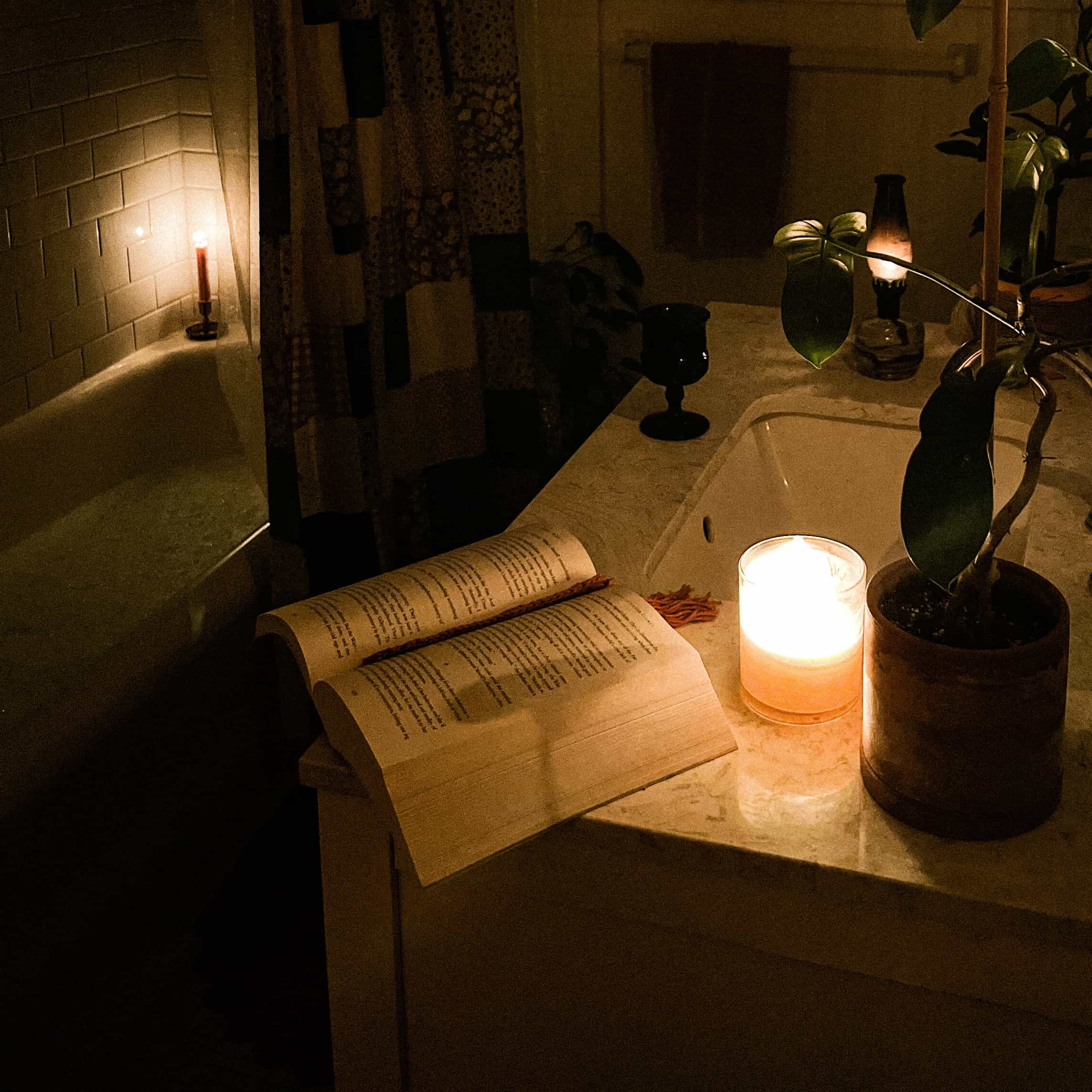 A dark, candlelit bathroom with an open book resting on the side of the sink.