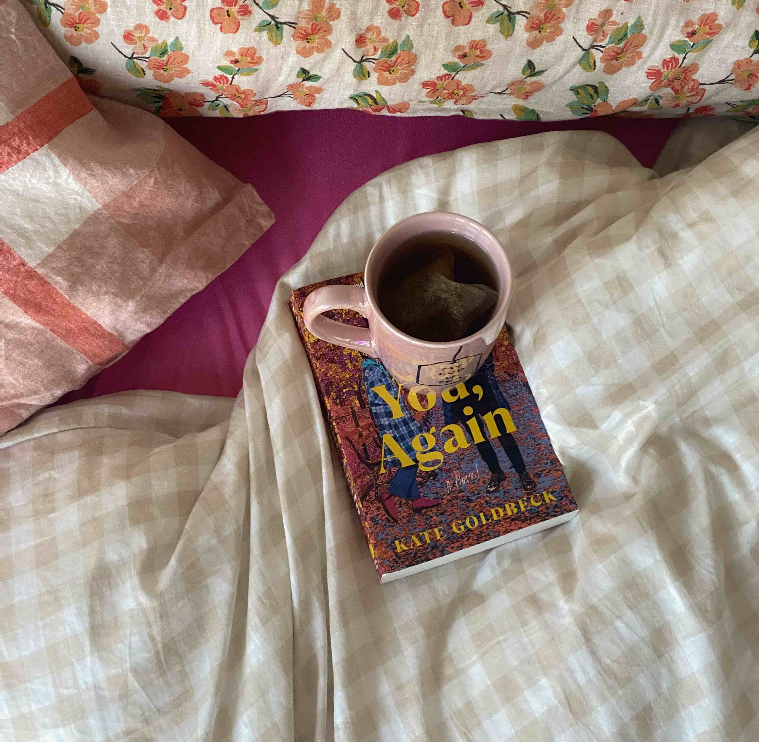 Cup of tea balanced on a book in pink and white bedsheets.
