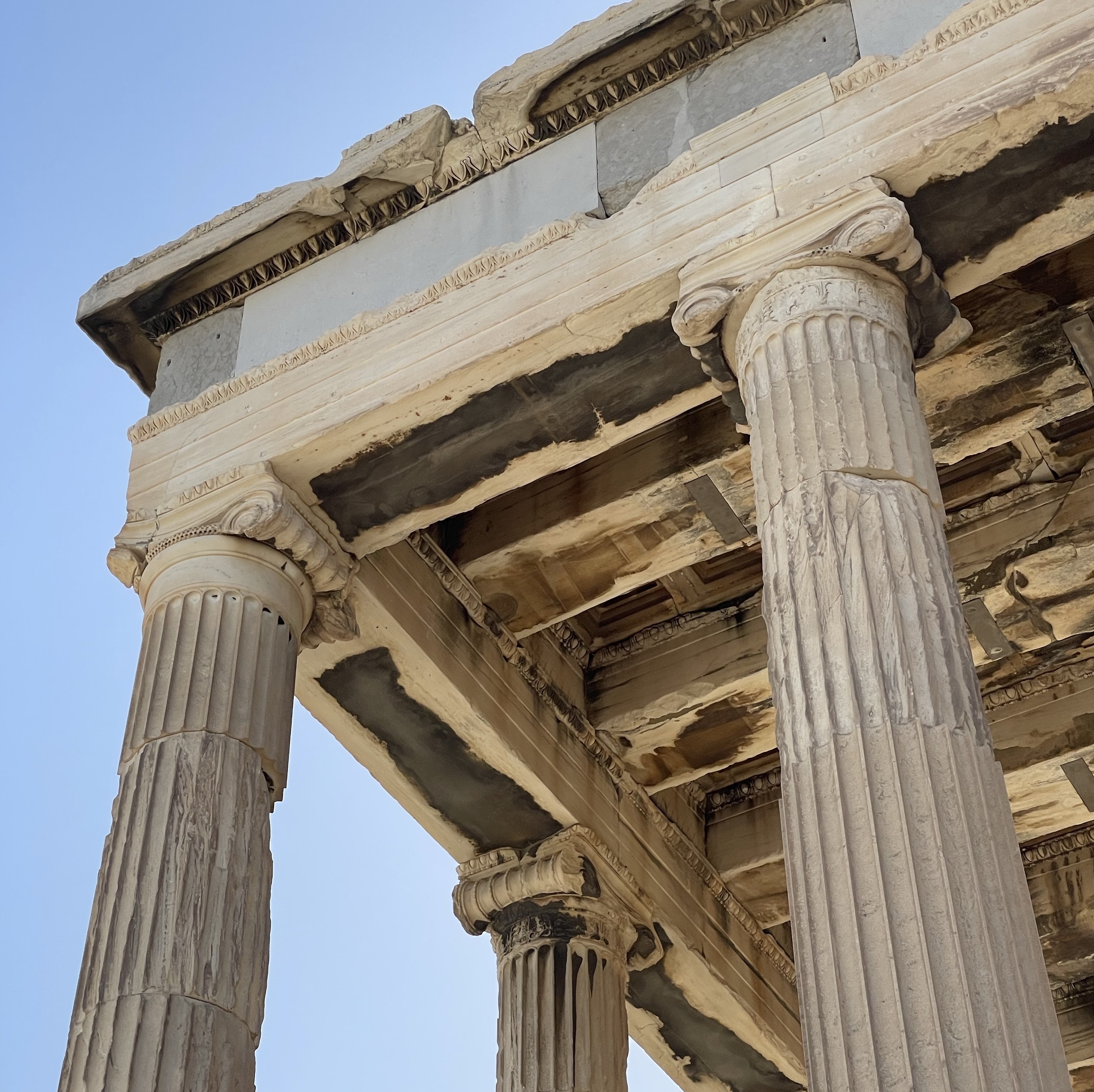 Close-up view of the ancient marble columns and ornate architecture of the Parthenon against a clear blue Greek sky.