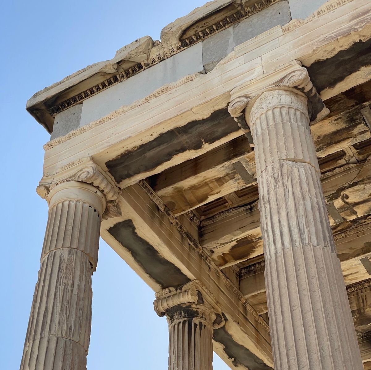 Close-up view of the ancient marble columns and ornate architecture of the Parthenon against a clear blue Greek sky.