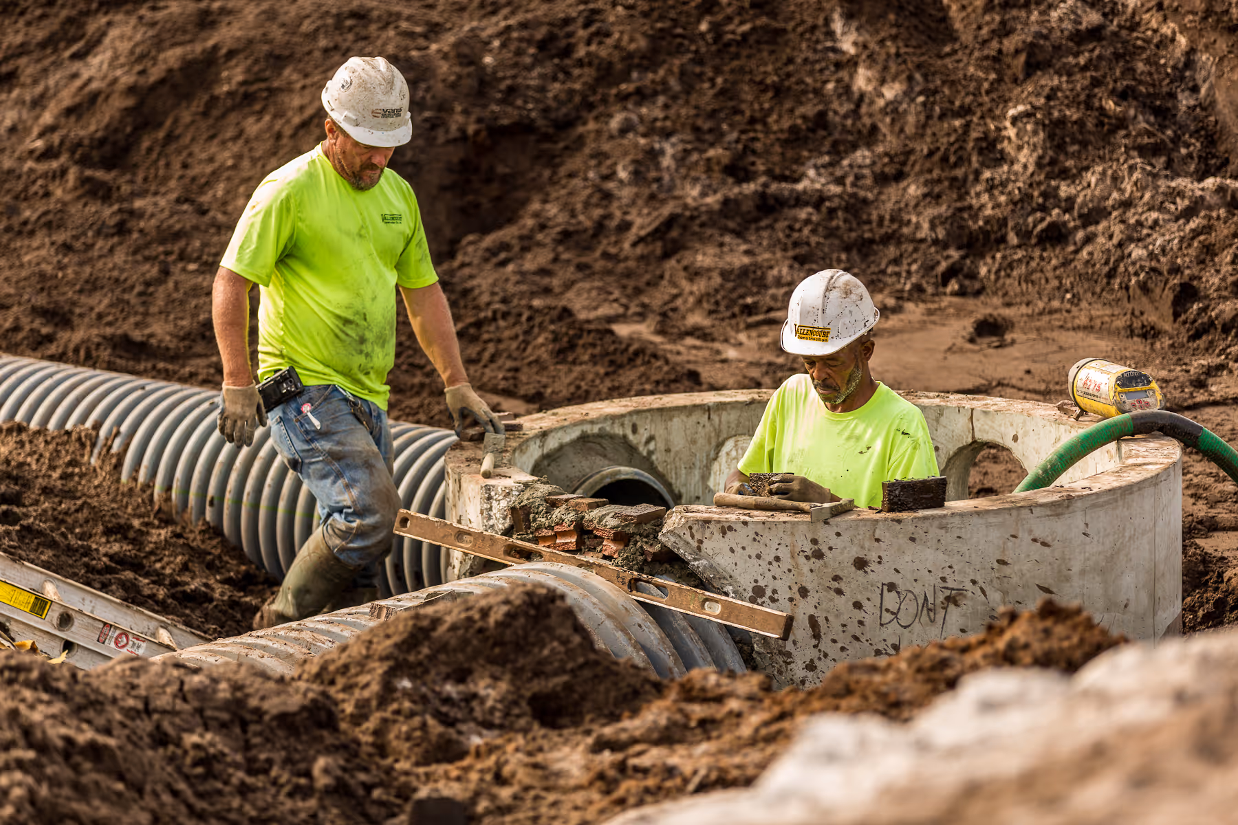 Construction workers installing drainage pipes in muddy excavation site