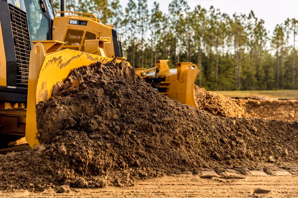 Yellow bulldozer moving large pile of dirt in forest construction site
