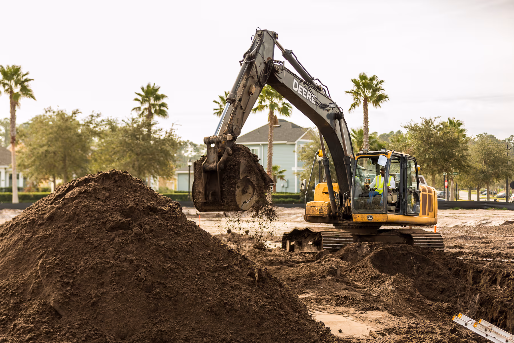 Excavator digging soil at construction site with palm trees in background