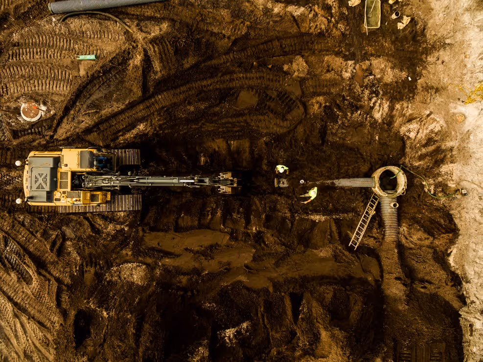 Excavator working in dark underground tunnel with rocky terrain