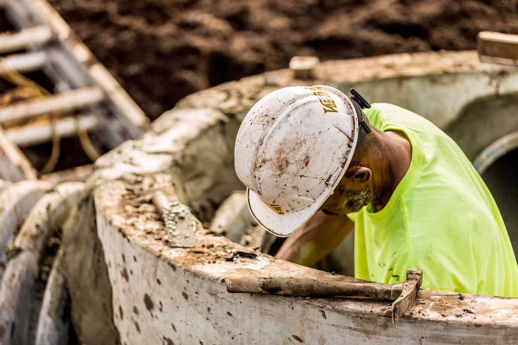 Construction worker in hard hat bends over concrete structure at worksite