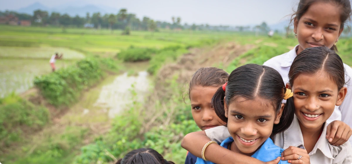 Group of smiling children with arms around each other in a green rural field.