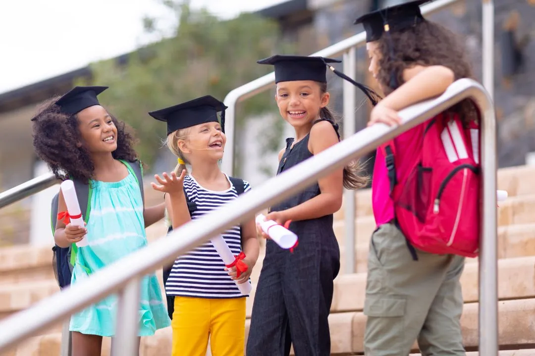 Young students in graduation caps holding rolled diplomas on school steps.
