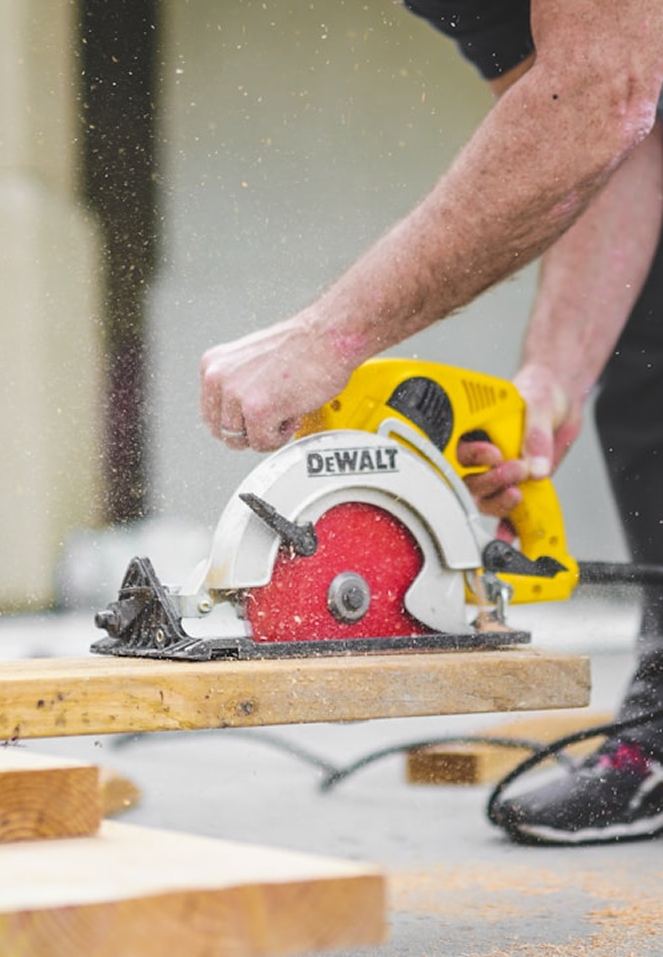 Man som använder Dewalt cirkelsåg för bygg entreprenad med hjälp av närliggande byggservice-utrustning.