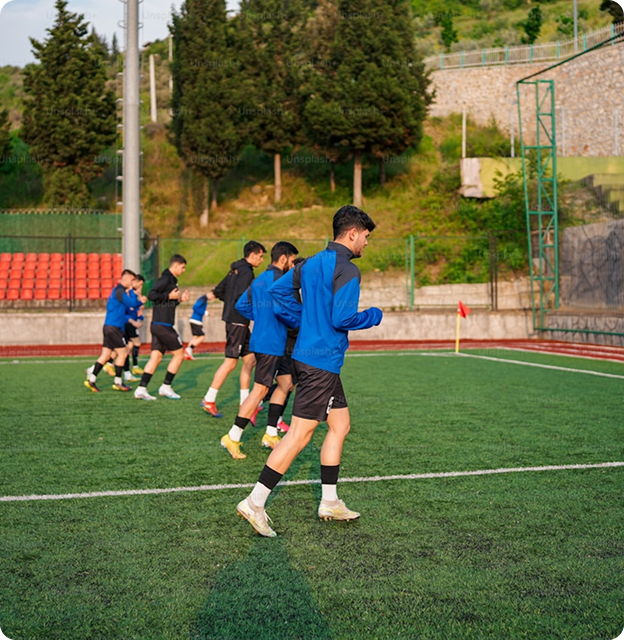 Fotbollsspelare tränar på planen i blå jackor och shorts med märket 'bygg'.