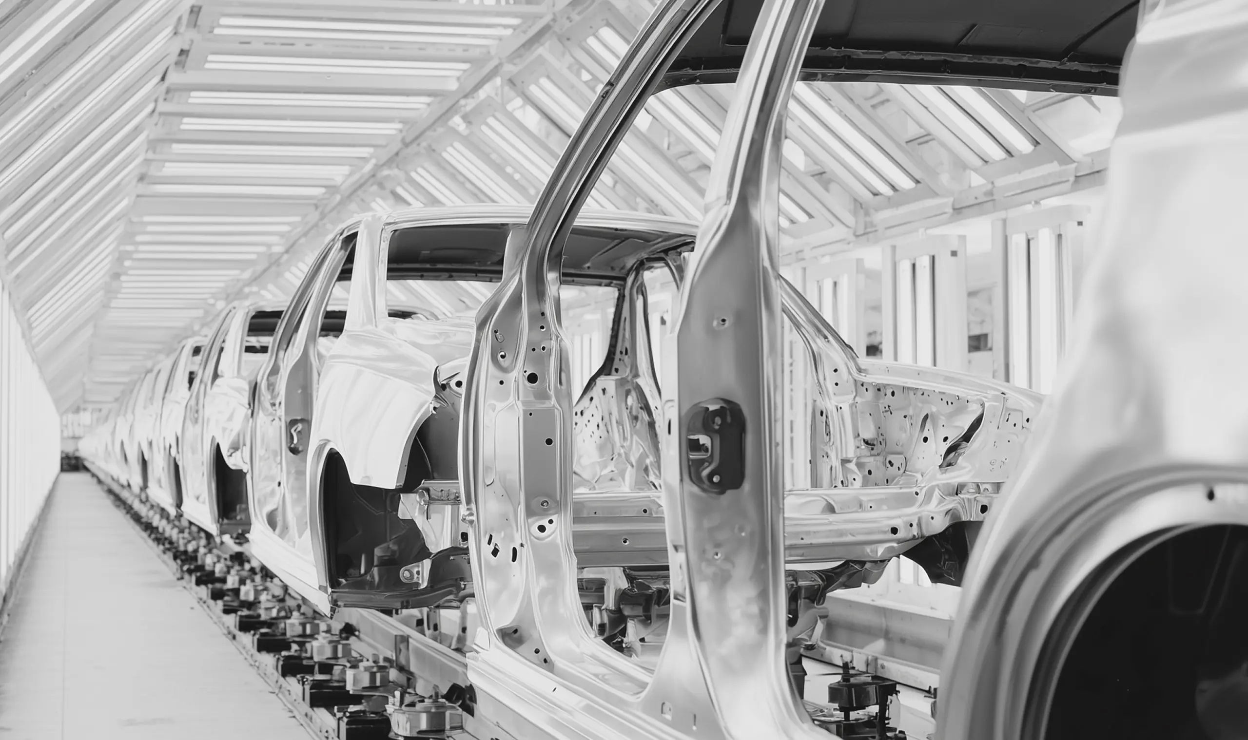 Row of car bodies on an assembly line inside a factory with bright overhead lighting.
