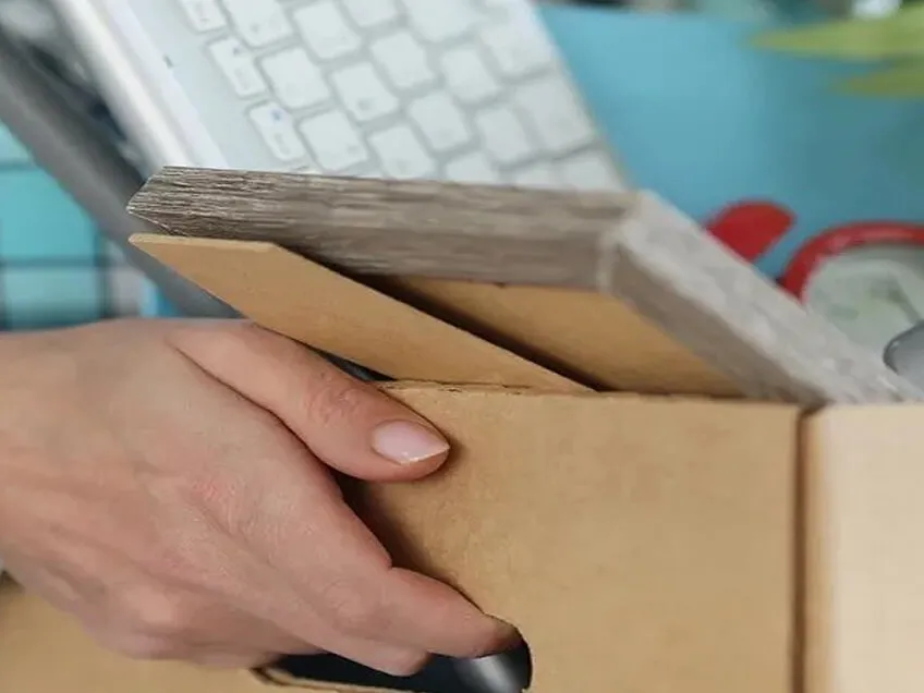 A hand placing office items into a cardboard box, representing someone being fired.