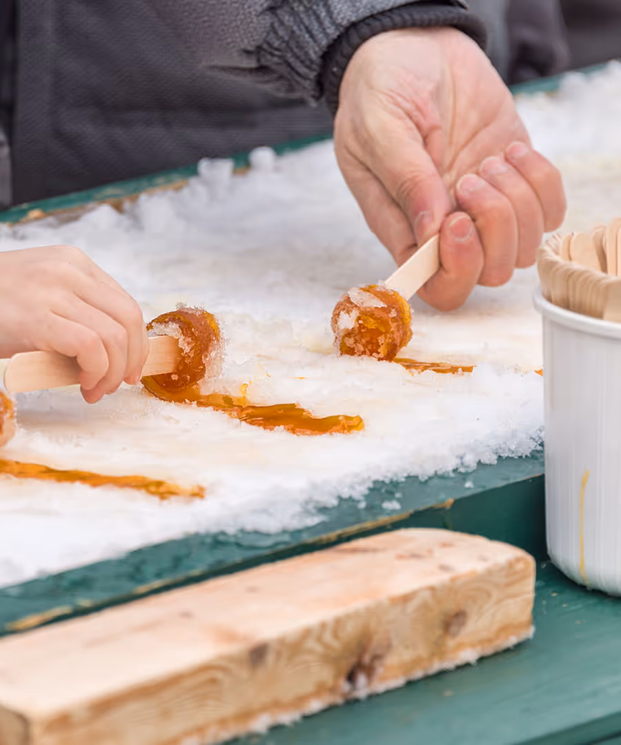 People rolling sugar on snow onto popsicle sticks