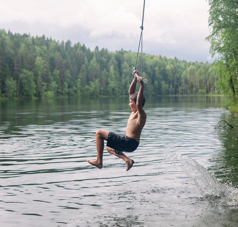 A boy hanging off a rope swing over the lake
