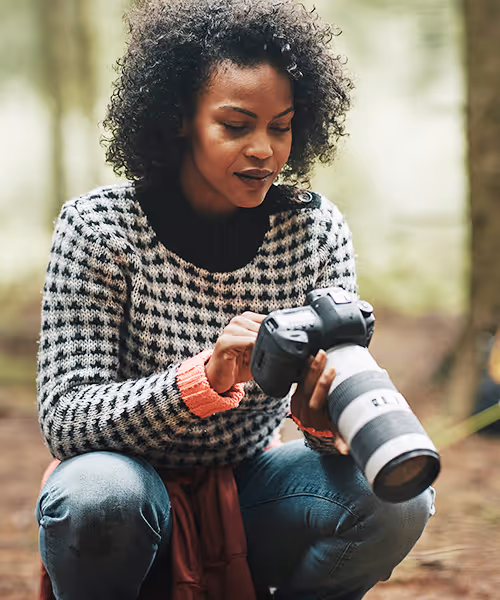 A woman in the woods looking through a professional camera