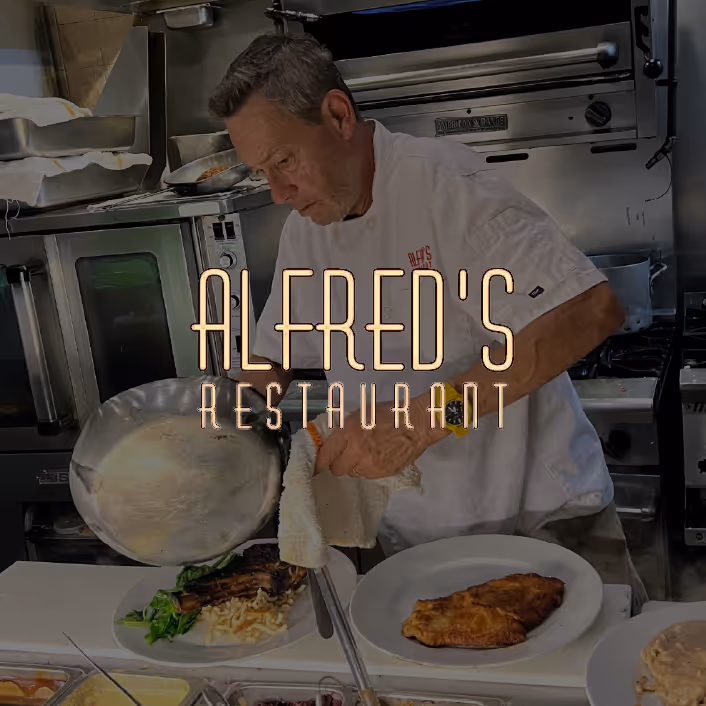 Chef in white uniform plating food in a professional kitchen with text overlay 'ALFRED'S RESTAURANT'.