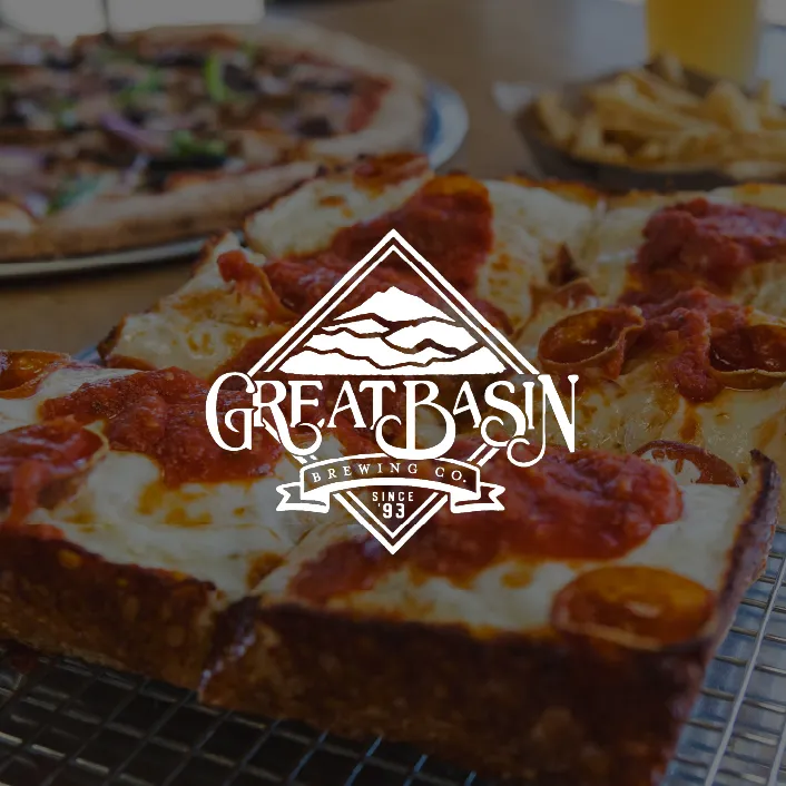 Close-up of a pepperoni pizza with tomato sauce and melted cheese on a wire rack, with another pizza and a plate of fries in the background.