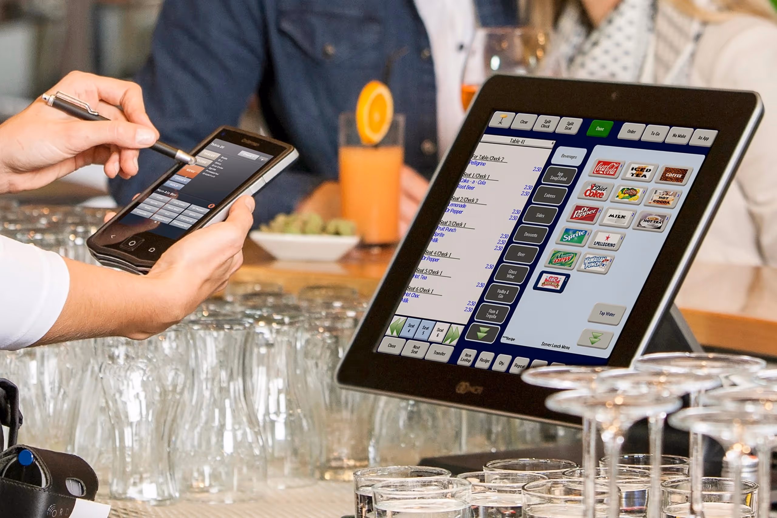 Person using a stylus to operate a handheld point-of-sale device next to a restaurant POS touchscreen with drink options.