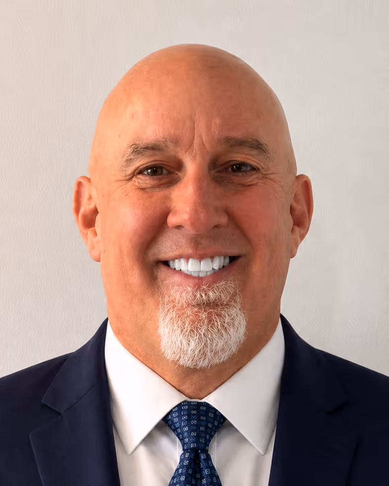Smiling bald man with a goatee, wearing a blue jacket over a pink collared shirt and glasses resting on his head.