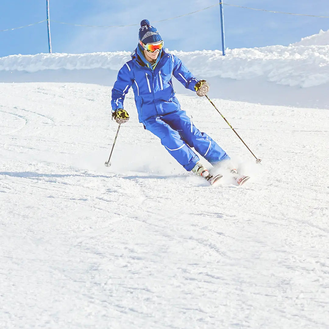 Person skiing downhill on fresh powder snow under clear blue skies, capturing winter recreation near Alcove at Midway.