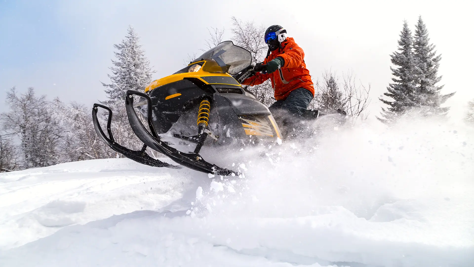 Man riding a snowmobile through deep snow in a winter forest near the luxury townhomes of Alcove in Midway, Utah