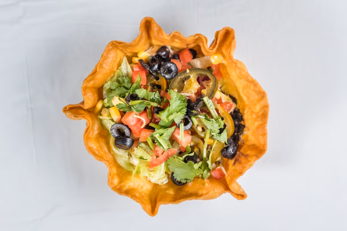 A bowl of food with a yellow crust and a variety of toppings.