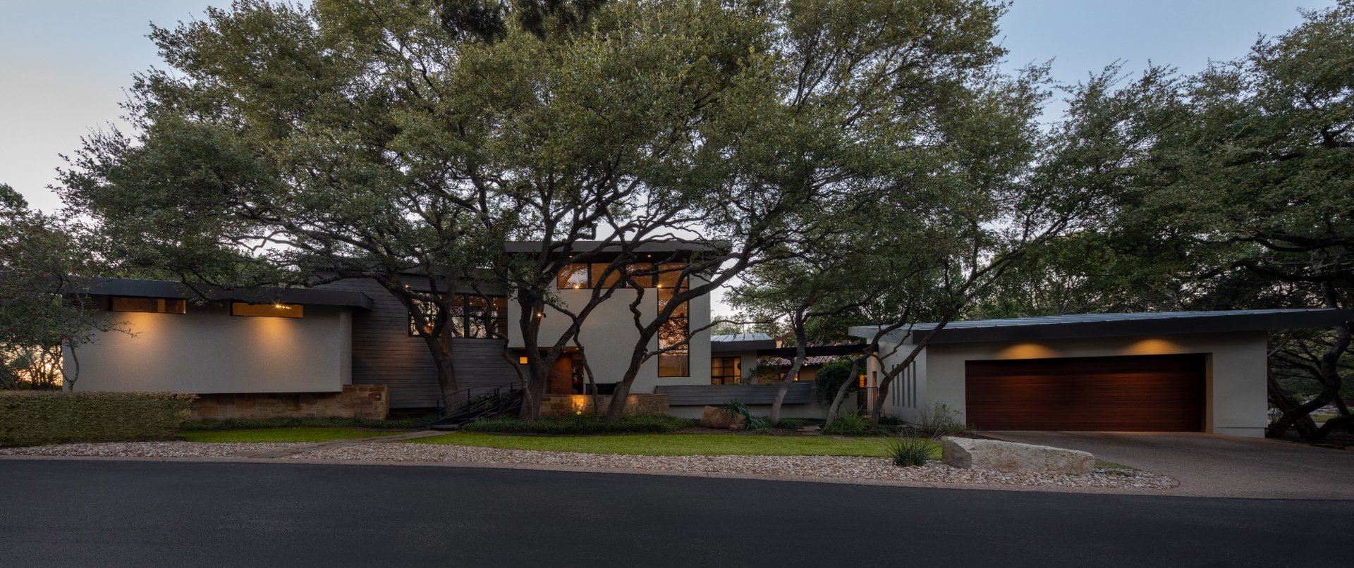 Panoramic exterior of a multi-million-dollar Austin home surrounded by mature oak trees.