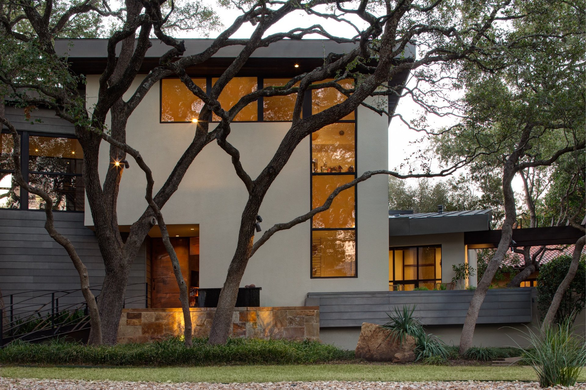 Side exterior of a luxury modern home with tall windows and natural stone elements.
