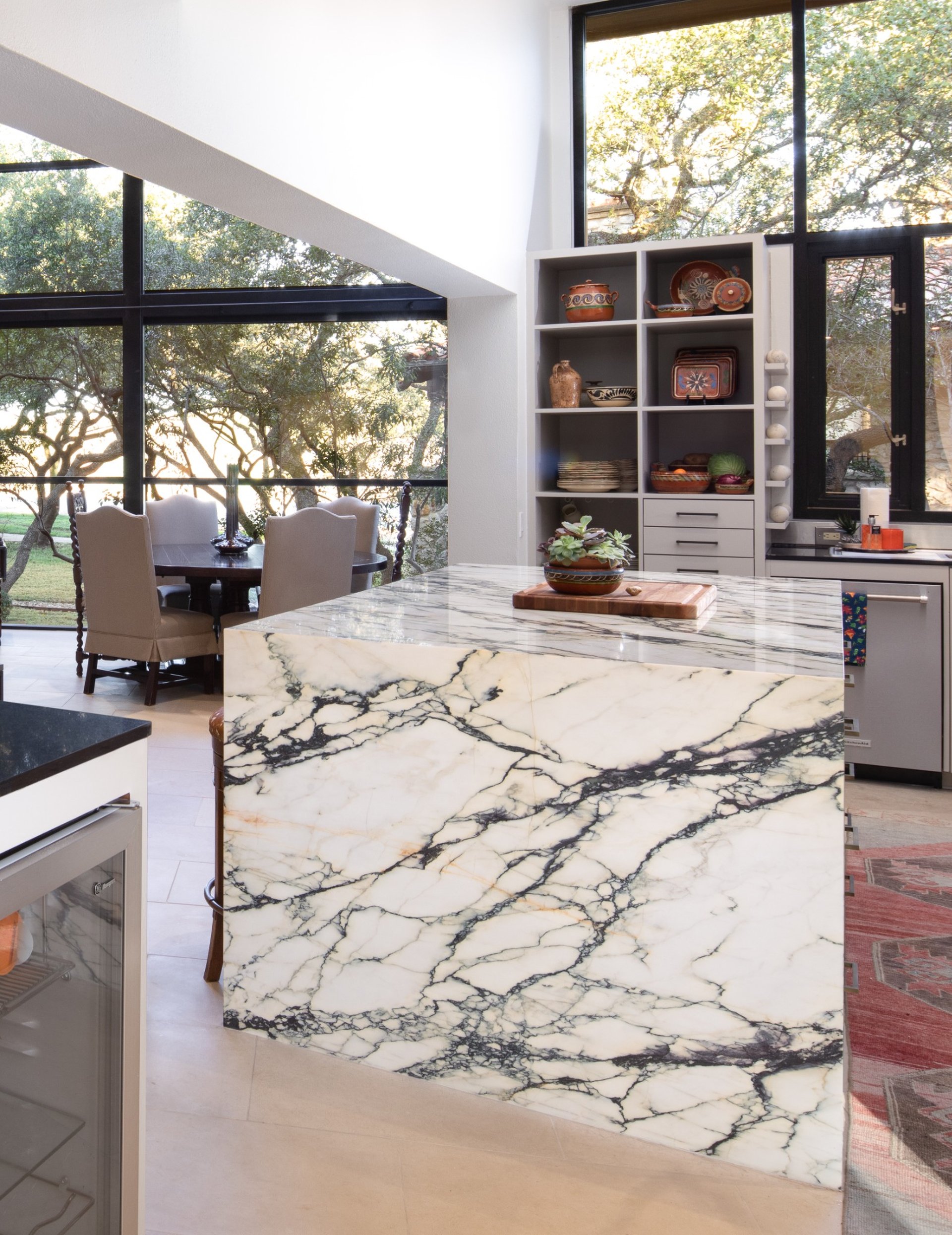 Elegant marble waterfall island in a modern kitchen with floor-to-ceiling windows.